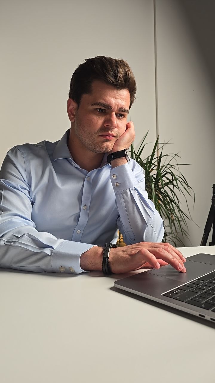 A thoughtful person seated at a laptop during a podcast or recording session.